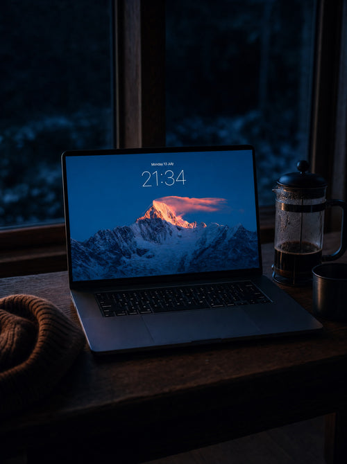 Alpenglow wallpaper on a MacBook Pro at a ski-lodge window desk before dawn