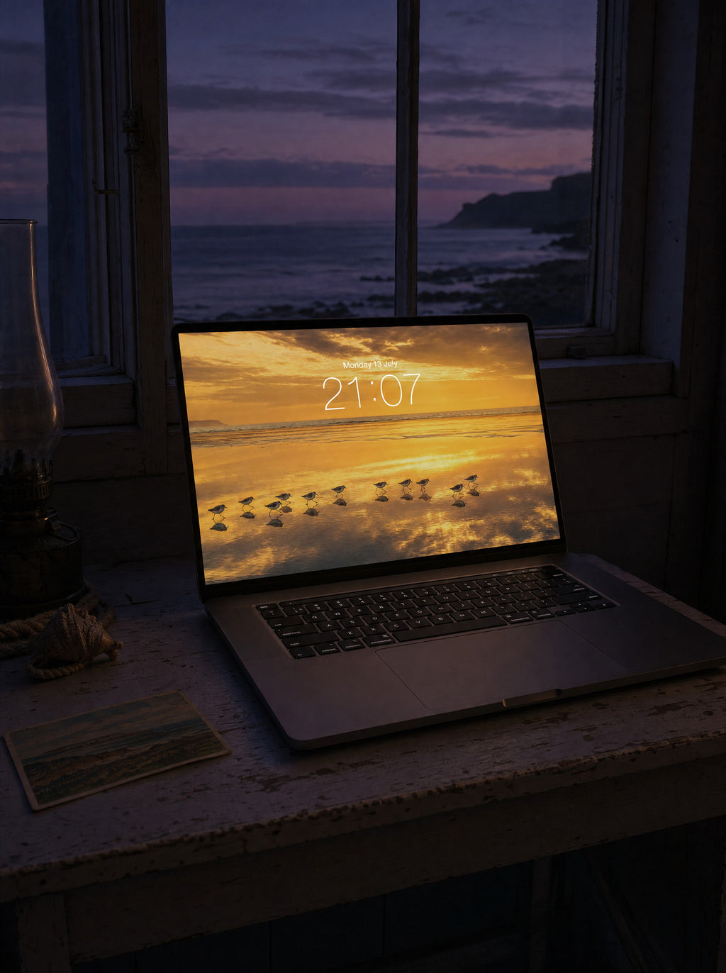 The Slow Tide wallpaper on a MacBook Pro at a coastal cottage desk at dusk